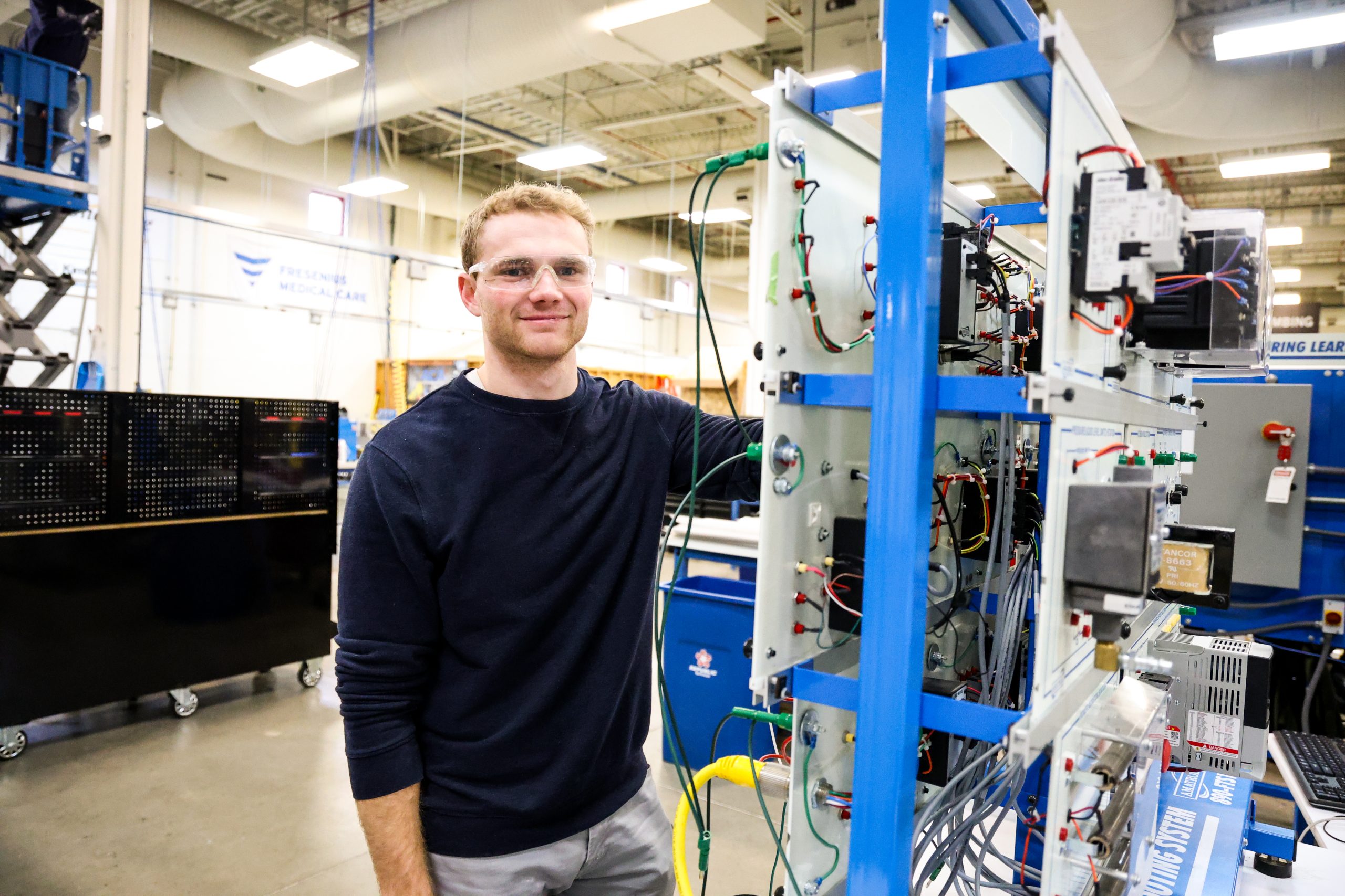 Student in OTECH's Automation Technology program smiling for a picture standing next to automation equipment.