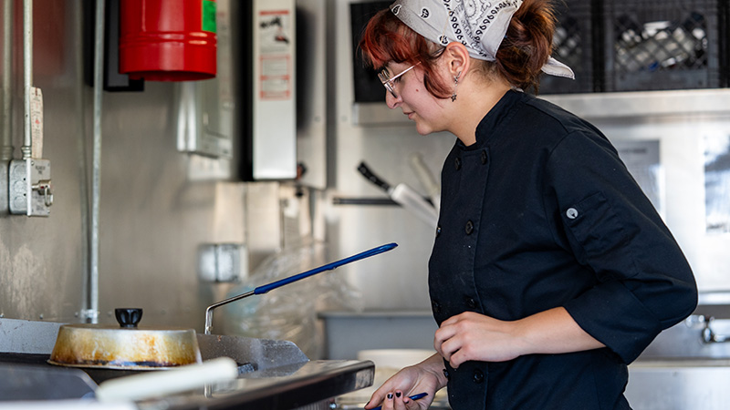 student working at a grill top cooking in the culinary arts program