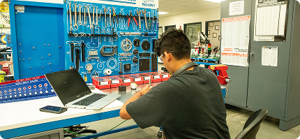 student with a laptop working at a desk with tools on a board in front of them
