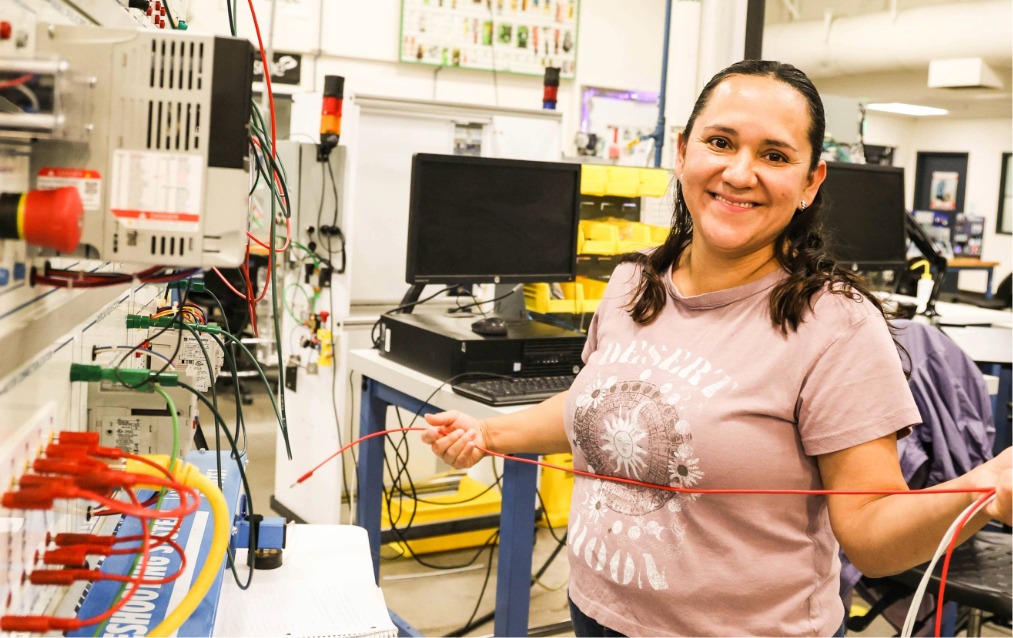 A student standing and smiling holding a wire in the manufacturing building at Ogden-Weber Technical College.