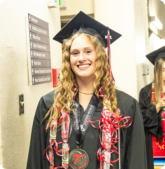 Young woman in red-trimmed graduation gown and cap smiles at camera.
