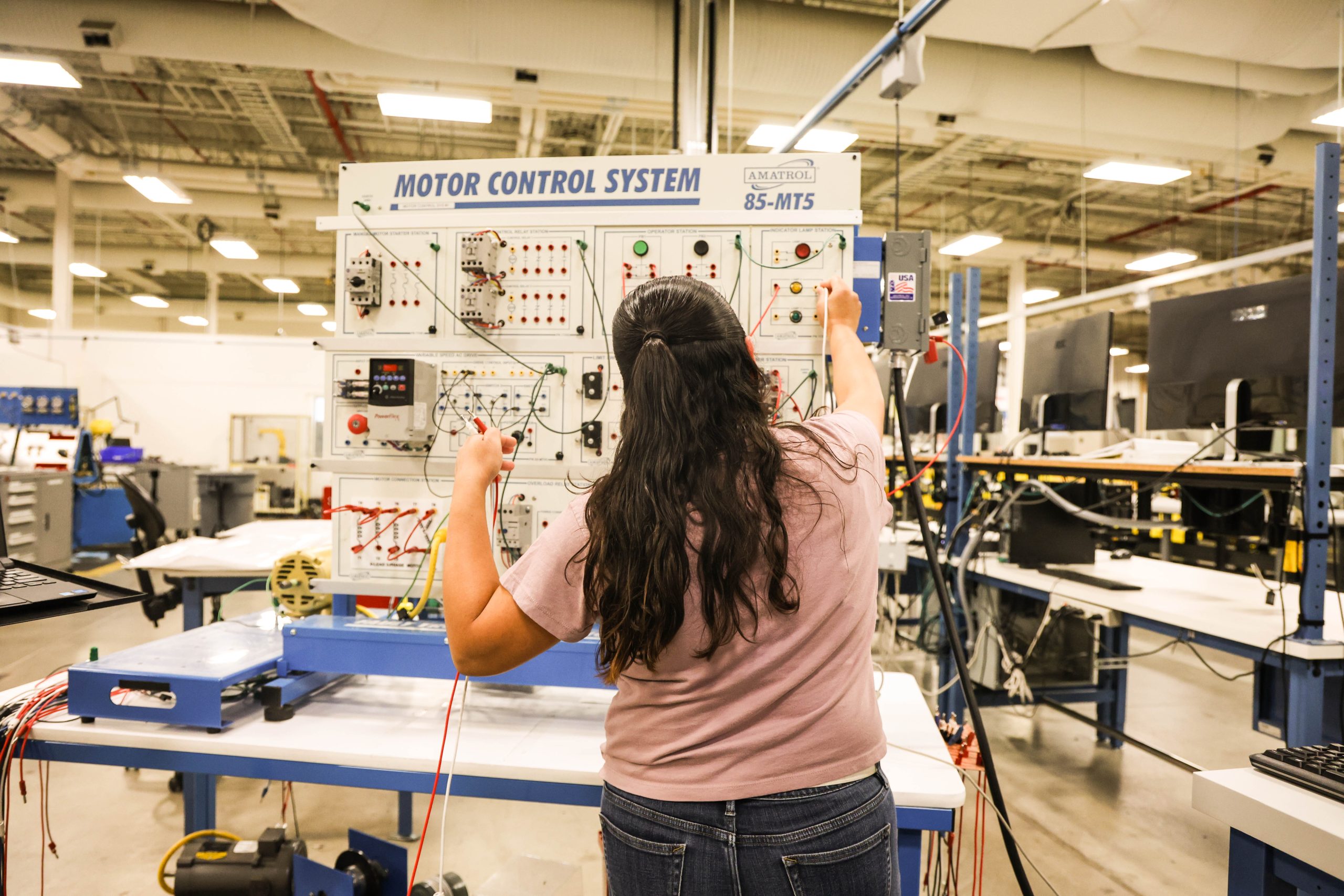 Student working with automation technology equipment, holding a wire inside the manufacturing building at Ogden-Weber Technical College.
