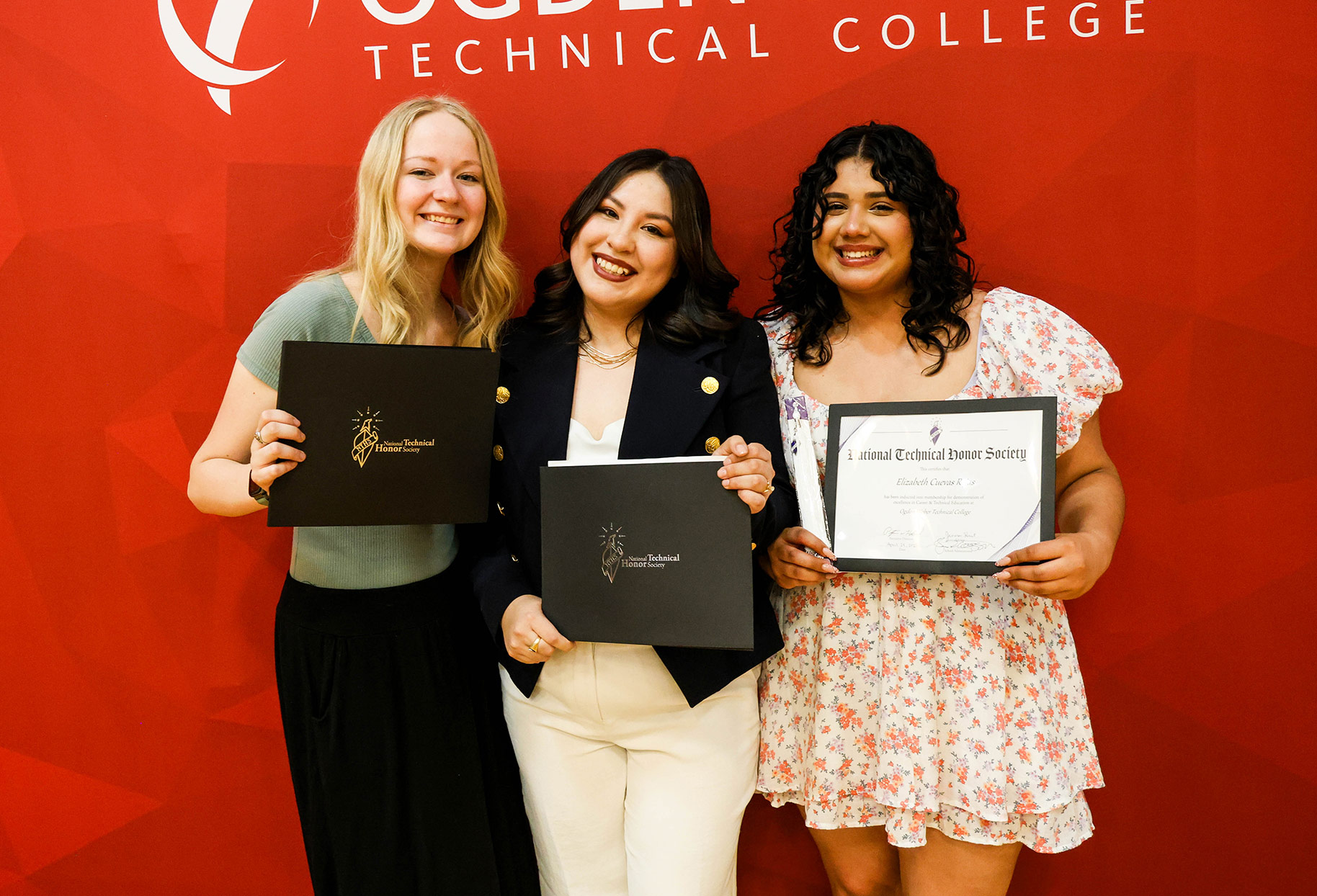 Three students holding National Technical Honor Society certificates in front of an Ogden-Weber Technical College banner