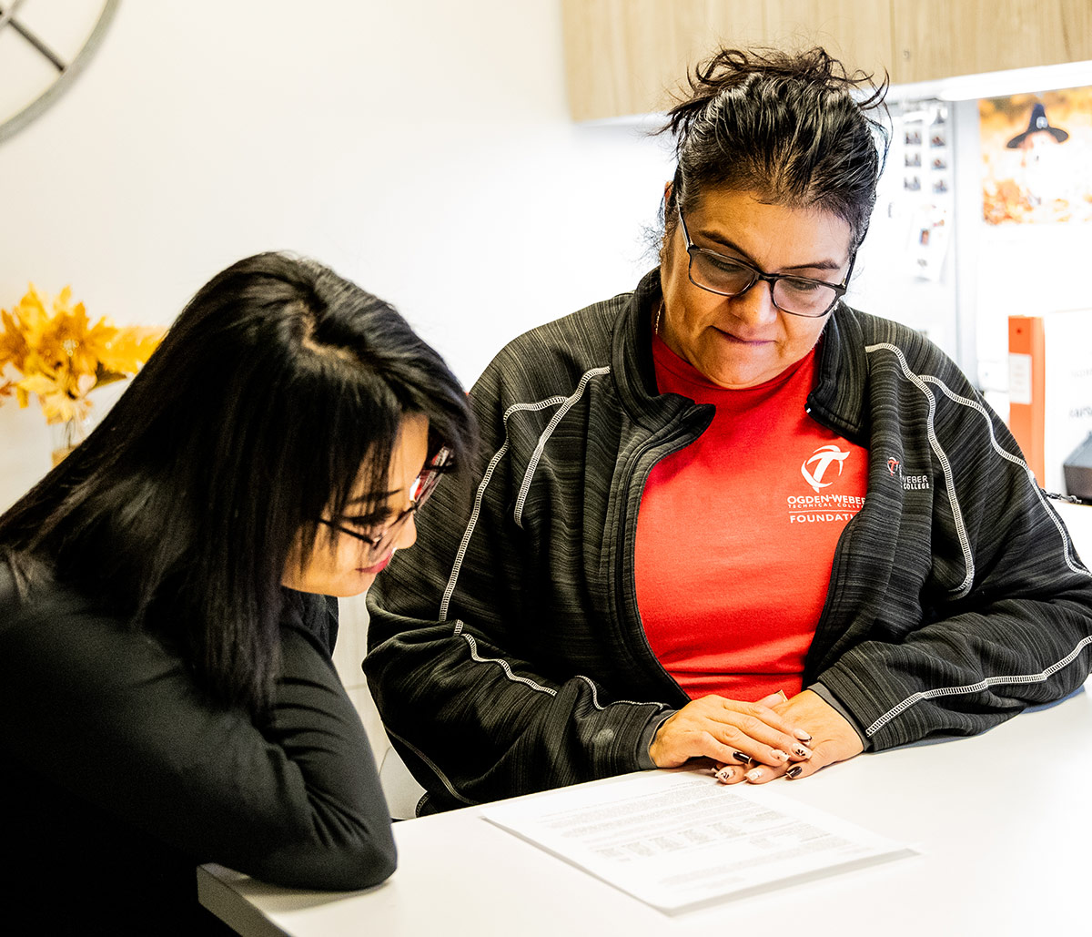 Ogden-Weber Technical College student support specialist in college gear assisting a student at a desk