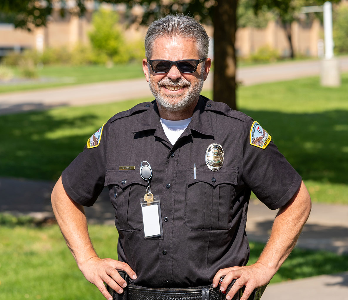 Smiling campus security officer in uniform with badge and sunglasses outdoors on campus